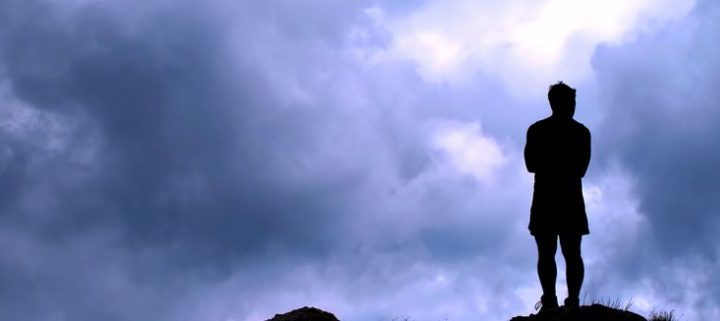 person standing on cliff looking at a cloudy yet peaceful sky